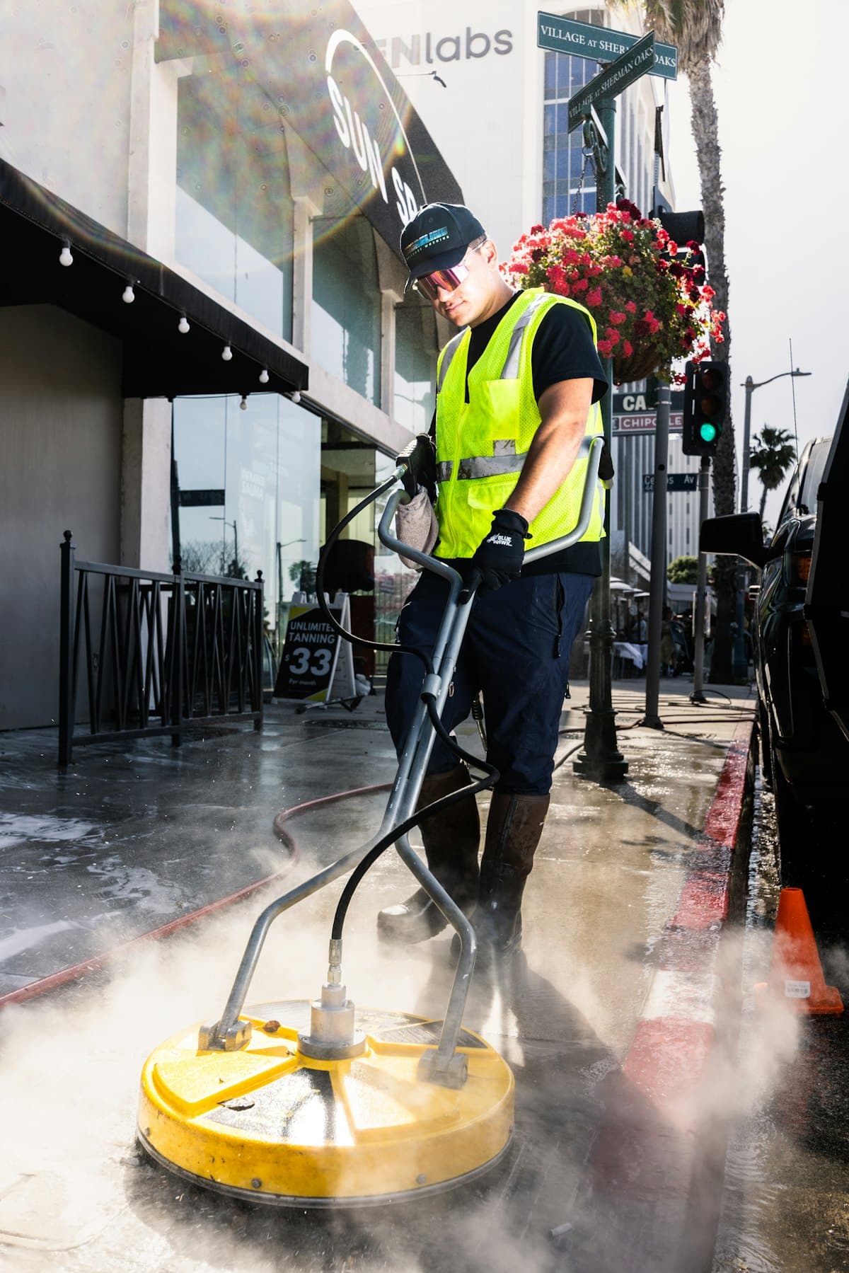 A worker in a high-visibility vest cleaning an outdoor paved area