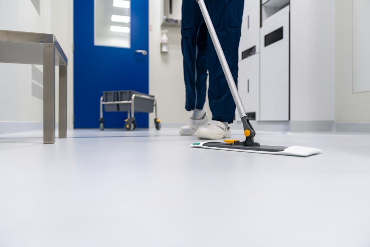 A cleaner in blue scrubs mopping a clinical hallway