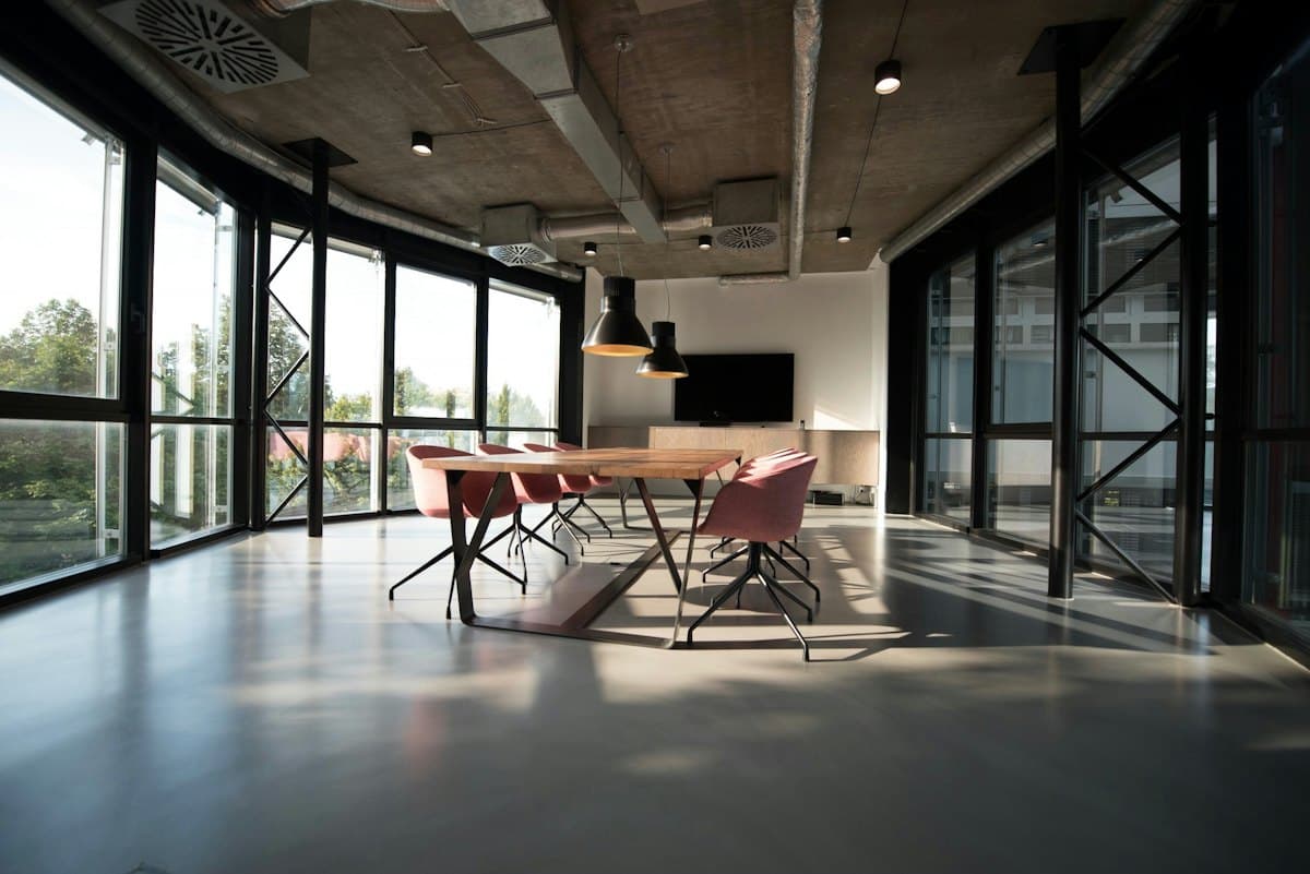An empty meeting room with a long table and chairs beside tall windows