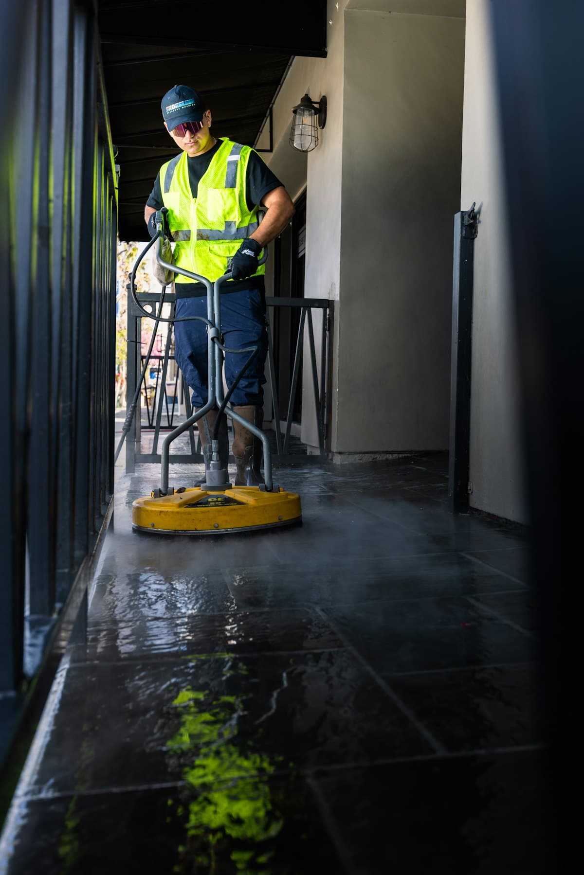 A maintenance worker in a high-visibility vest cleaning a paved outdoor area